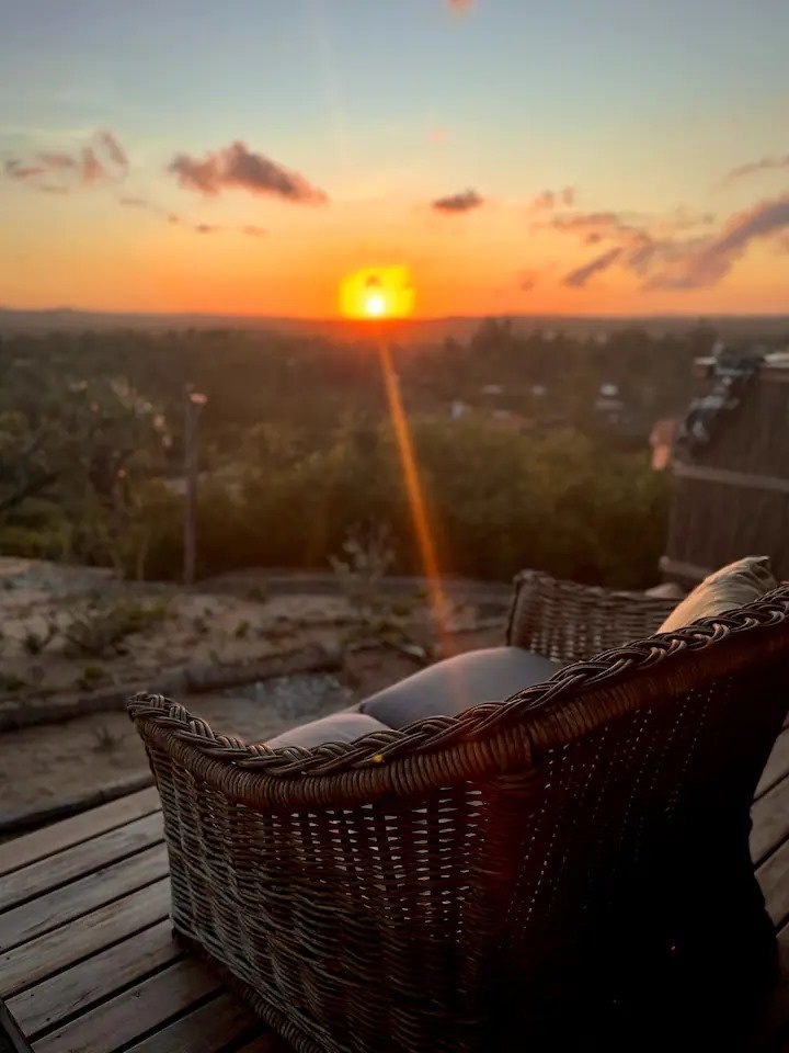 Pôr do sol visto de uma varanda com cadeira de vime